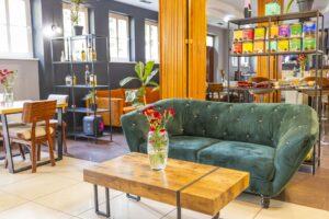 zielona kanapa przy małym drewnianym stoliku, czerwone kwiaty w dużym wazonie na stole