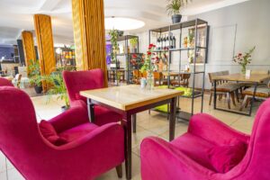 różowe fotele przy małym stoliku, kwiaty, w tle regały i kolejne stoły