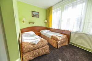 pokój z zielonymi ścianami, dwa łóżka pojedyncze, obraz i lampy na ścianie