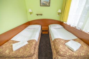 pokój z zielonymi ścianami, dwa łóżka pojedyncze, obraz i lampy na ścianie