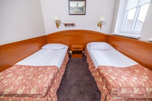 dwa łóżka pojedyncze, obraz i dwie lampy na ścianie