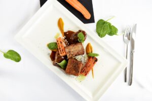 potrawa mięsna na białym prostokątnym talerzu, obok sztućce